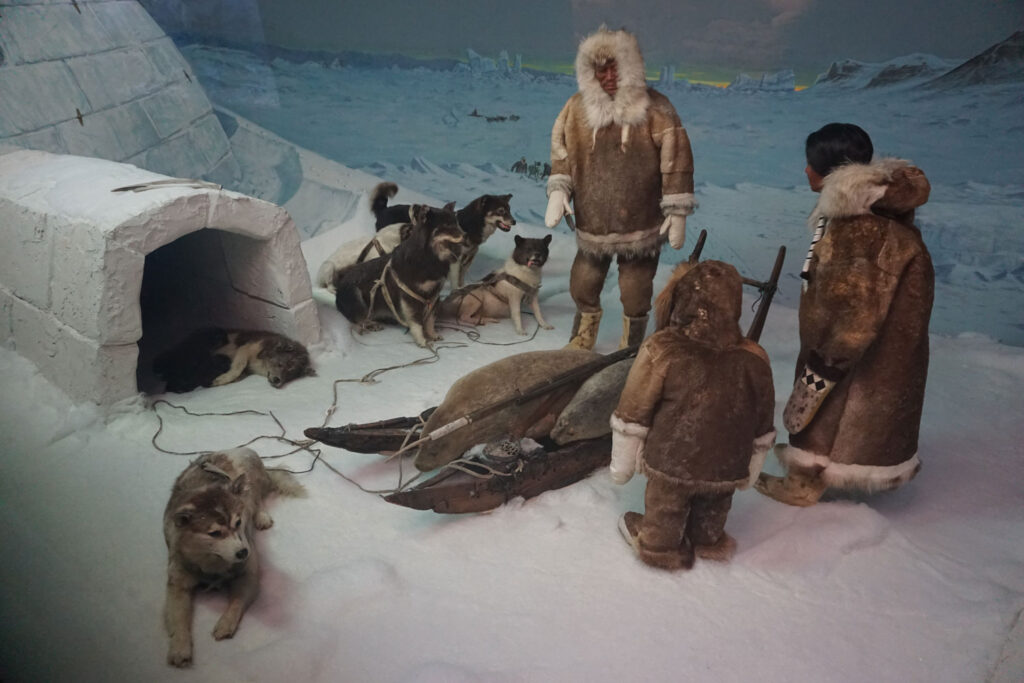 Inuit stehen vor einem Iglu mit einem Hundeschlitten